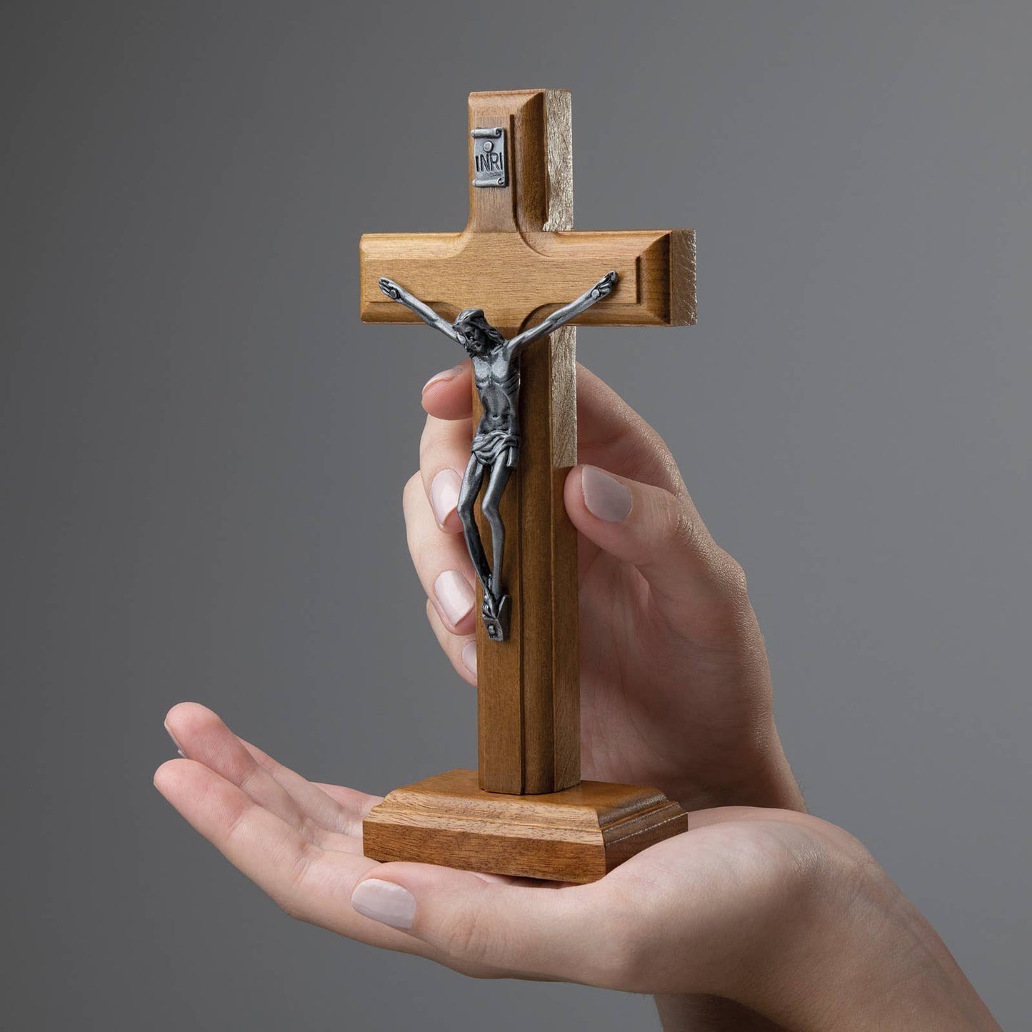 Wooden cross with a silver figure held in a hand against a gray background