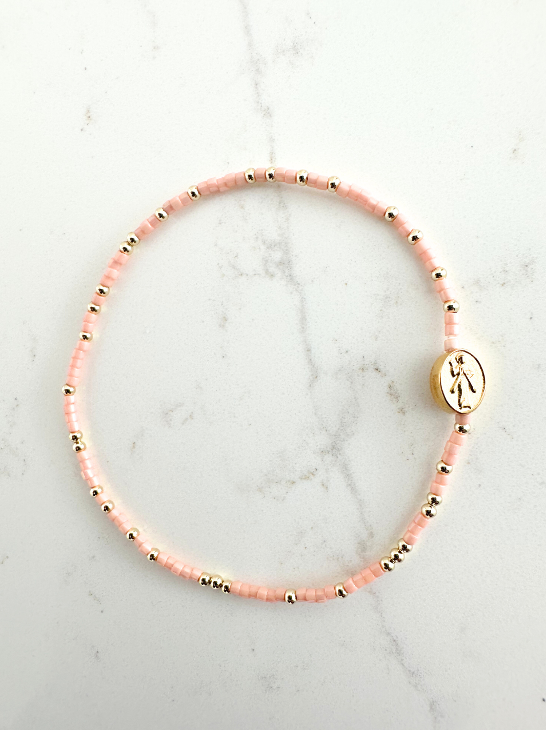 Pink beaded bracelet with a gold charm on a marble surface