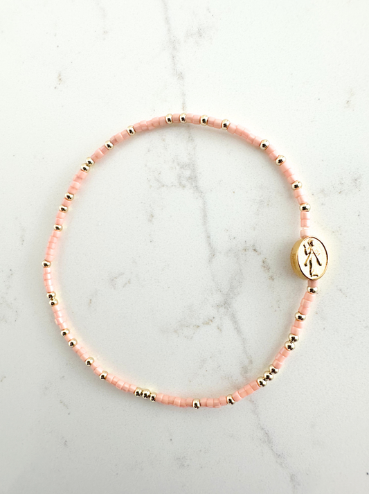 Pink beaded bracelet with a gold charm on a marble surface