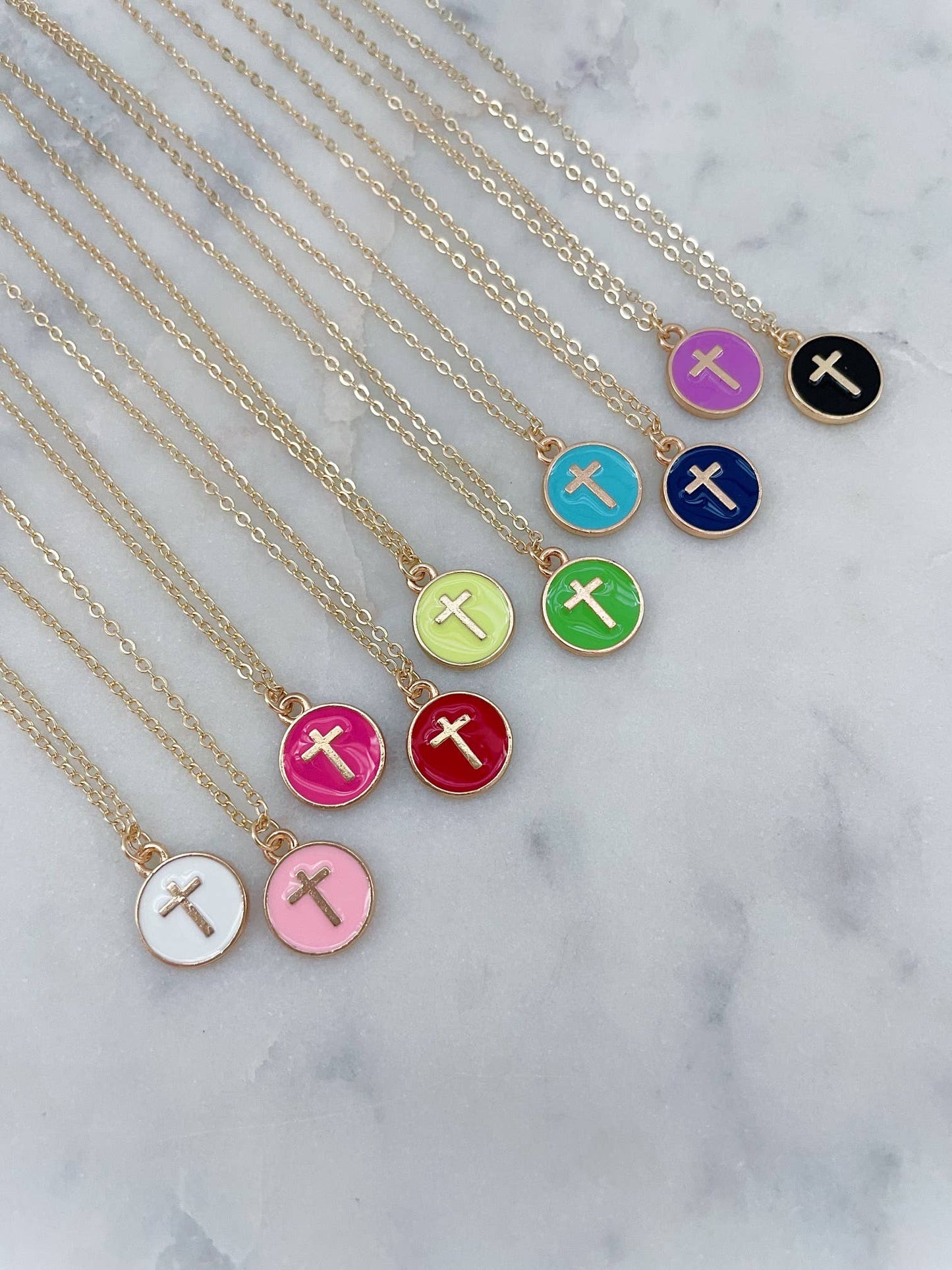 Necklaces with colorful circular pendants featuring crosses on a marble surface