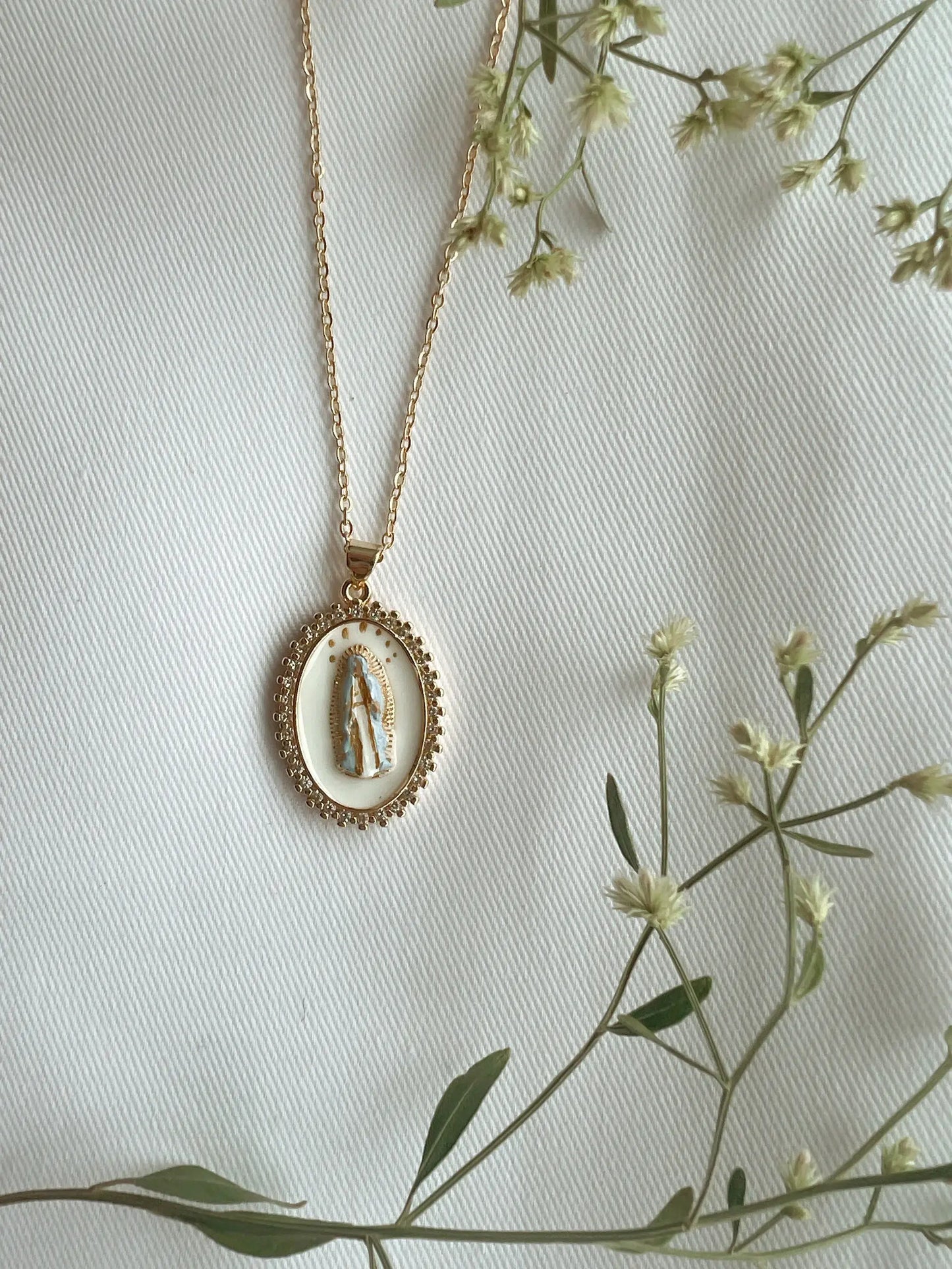 Gold necklace with a pendant on a light background with greenery