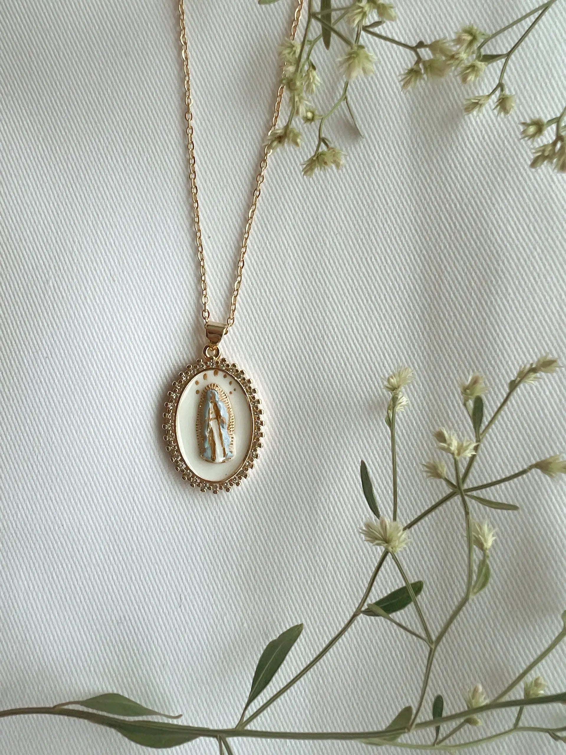 Gold necklace with a pendant on a light background with greenery