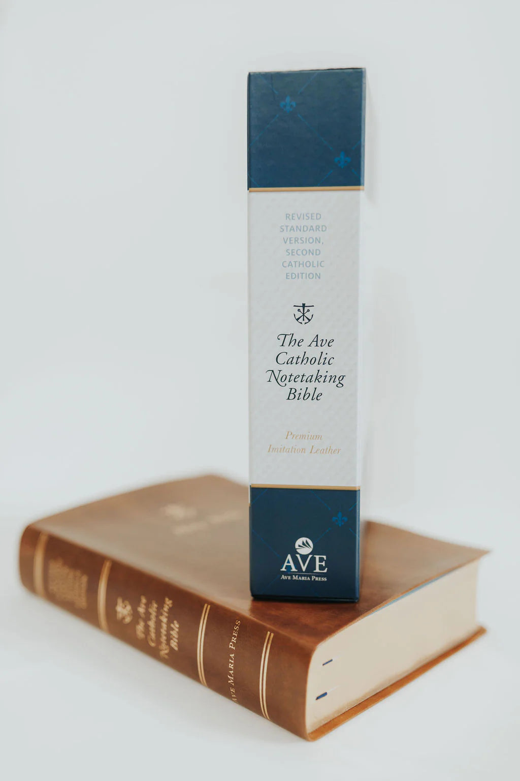 The Ave Catholic Nuptiating Bible by Ave Bible Press, standing upright on top of a brown leather-bound Bible against a clean white background.