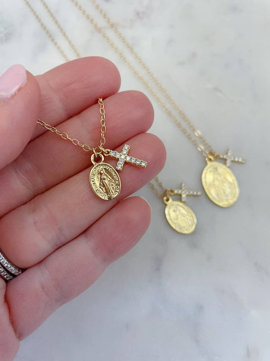 Gold necklaces with religious pendants held by a hand on a marble background
