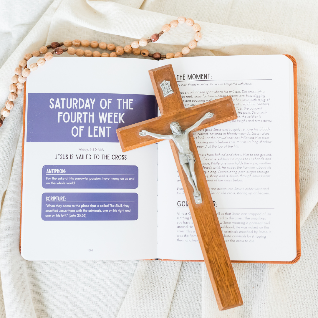 Open book with a wooden cross and rosary on a light fabric background