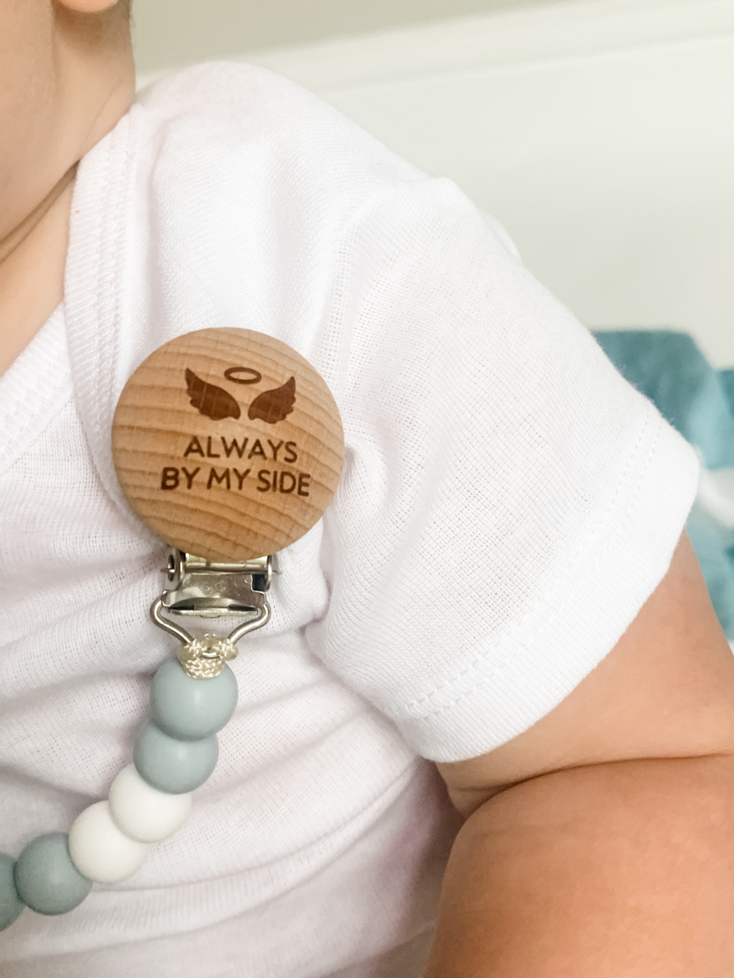 Wooden pacifier clip with engraved text on a white blanket