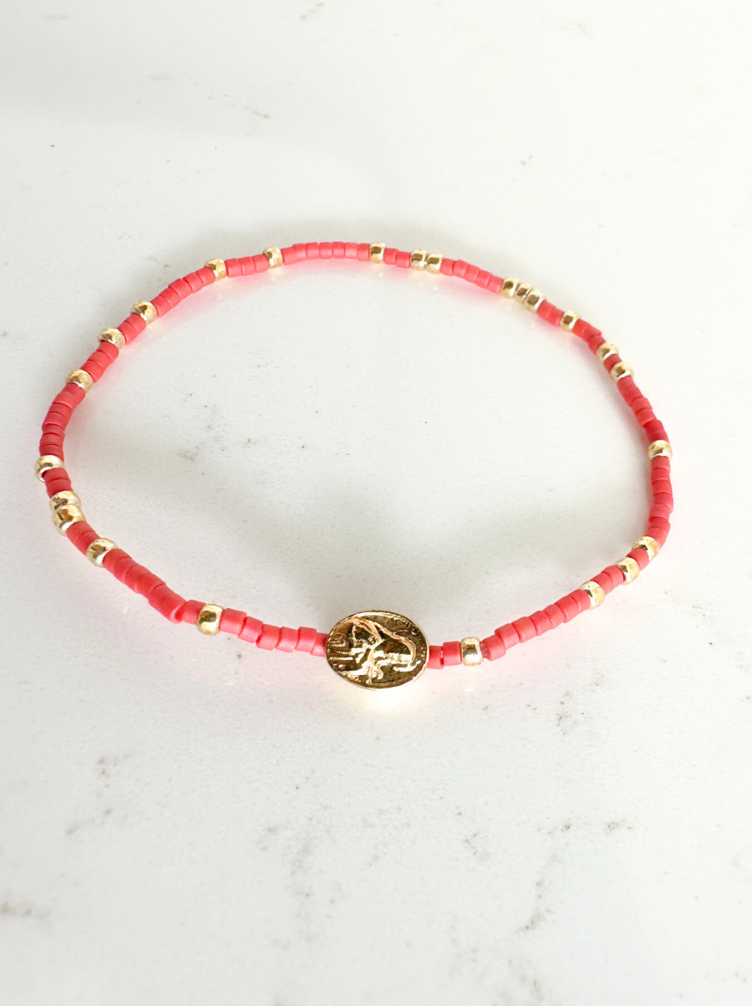 Red beaded bracelet with gold accents on a white marble surface