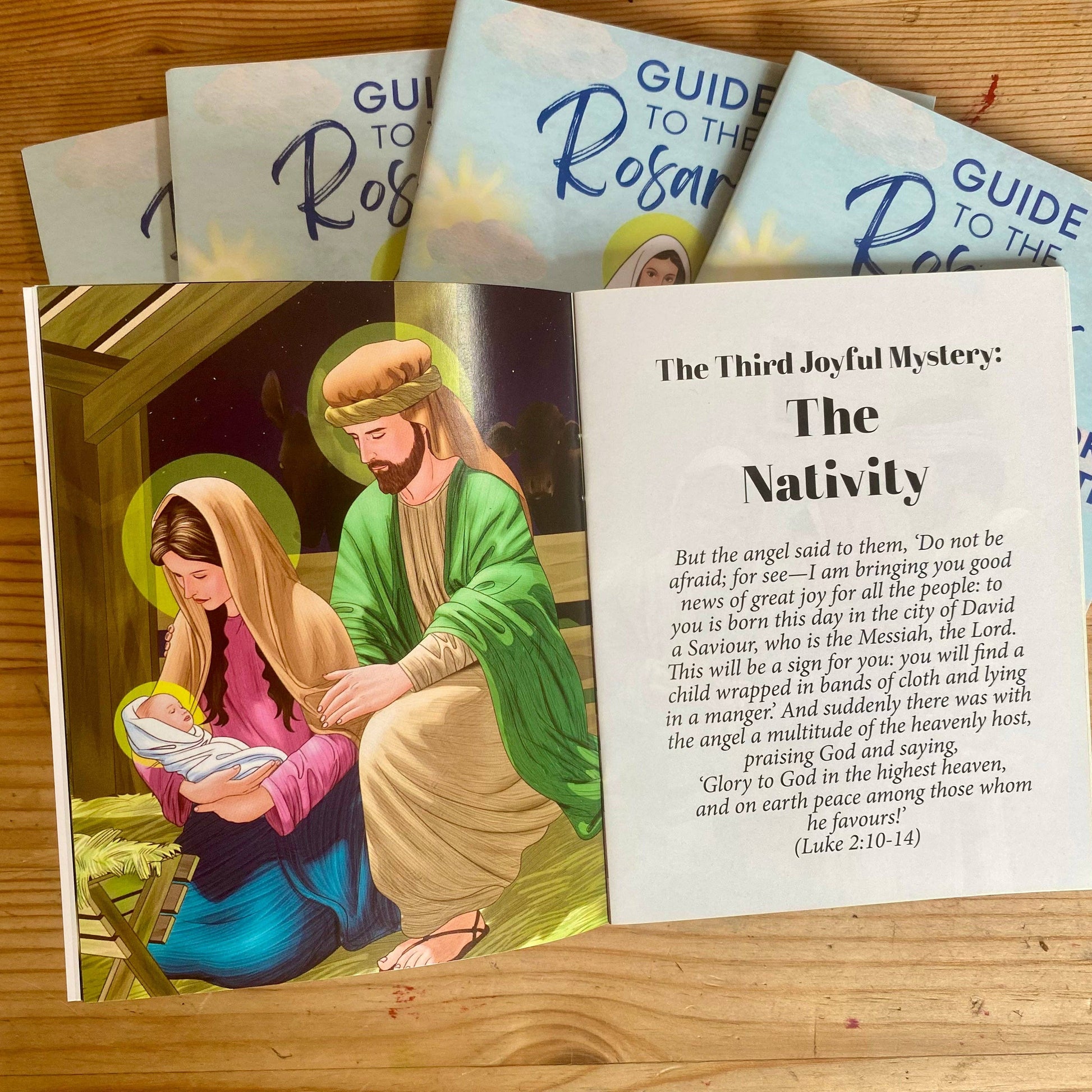 Booklets titled 'Guide to the Rosary' on a wooden surface with an illustration of the Nativity scene.