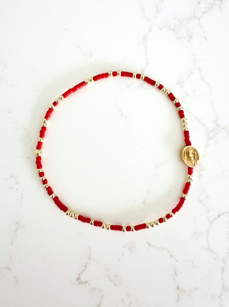 Red beaded bracelet with gold accents on a white marble surface