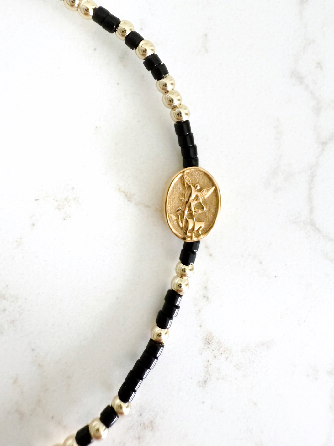 Black and gold beaded bracelet with a pendant on a white marble background