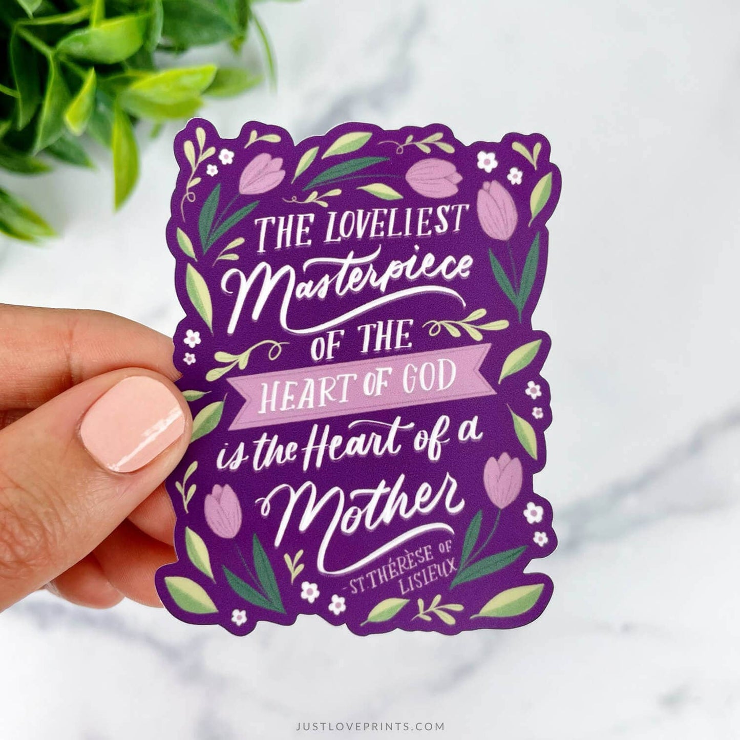 Purple decorative sticker with floral design and text held by a hand on a white background.
