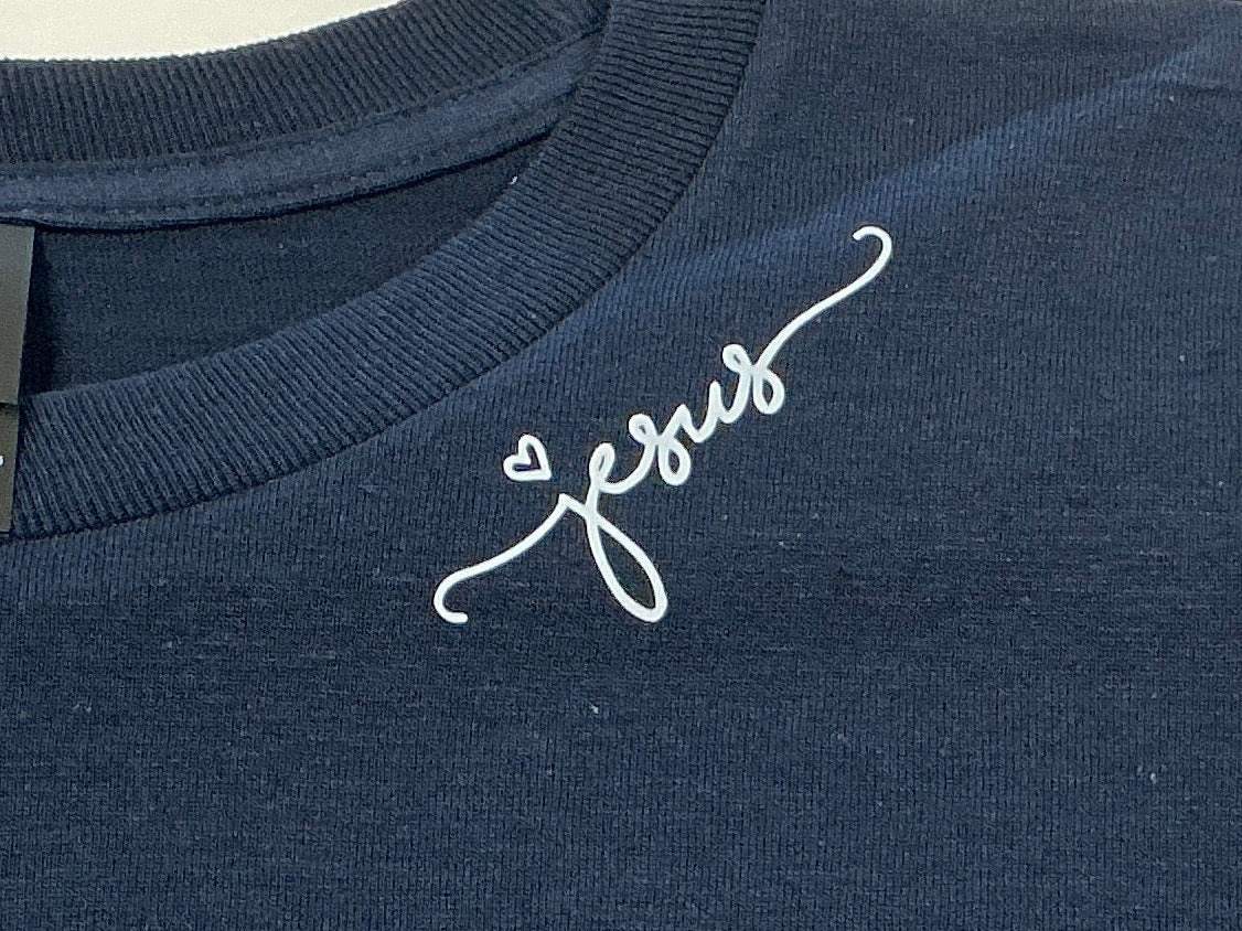 Navy blue shirt with 'Jesus' on it in white on a plain background