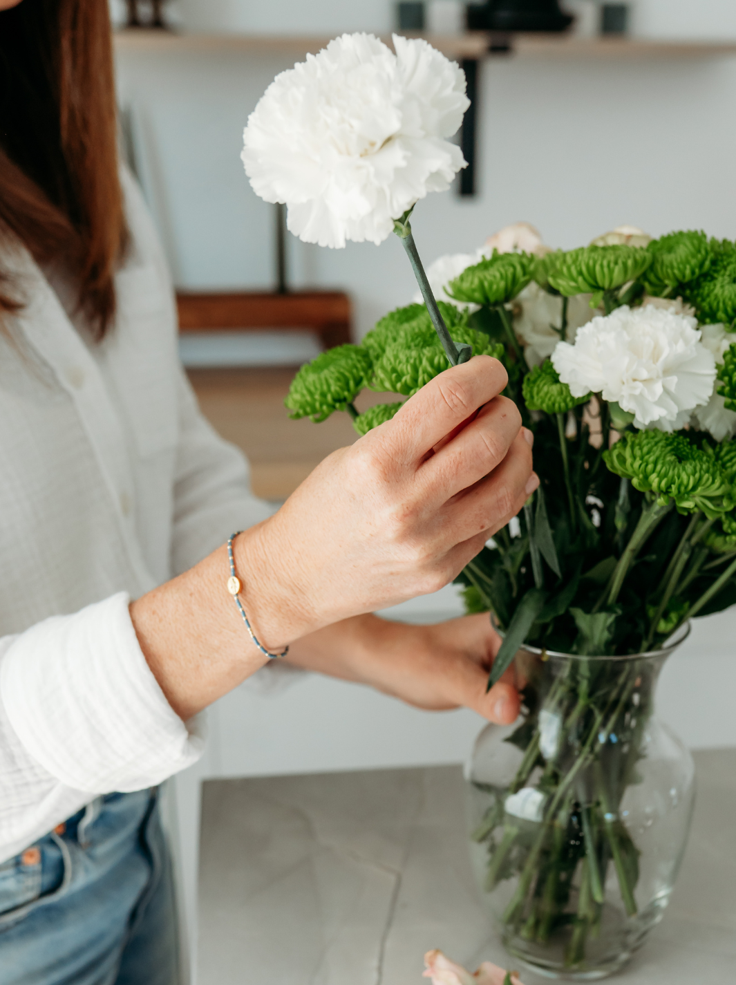 Person arranging flowers in a vase with a blurred indoor background