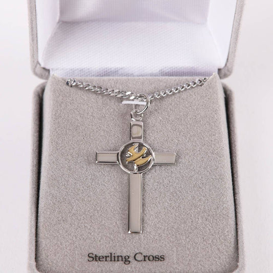 Silver cross pendant with a gold emblem on a gray cushion in a jewelry box.