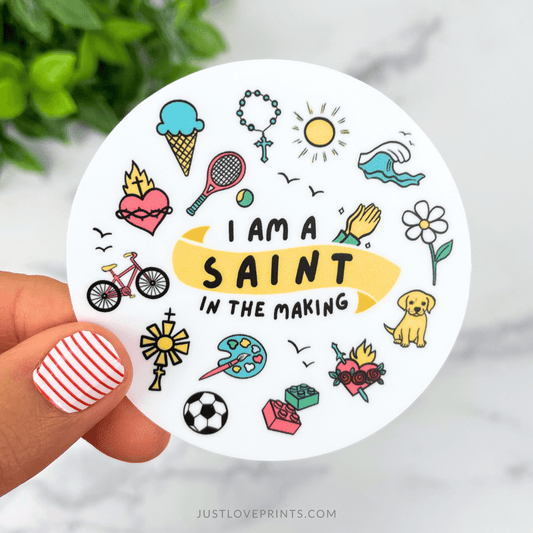 Circular sticker with illustrations and text 'I am a saint in the making' held by a hand.