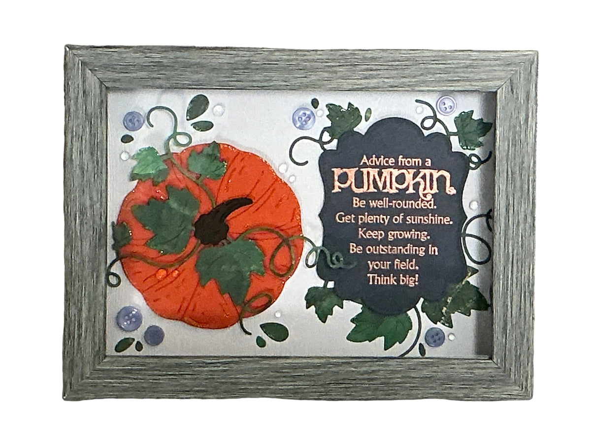A framed autumn-themed art piece featuring a 3D orange pumpkin with green leaves next to a dark slate sign that reads 'Advice from a pumpkin' with inspirational text, set in a distressed gray wooden frame against a textured gray background.