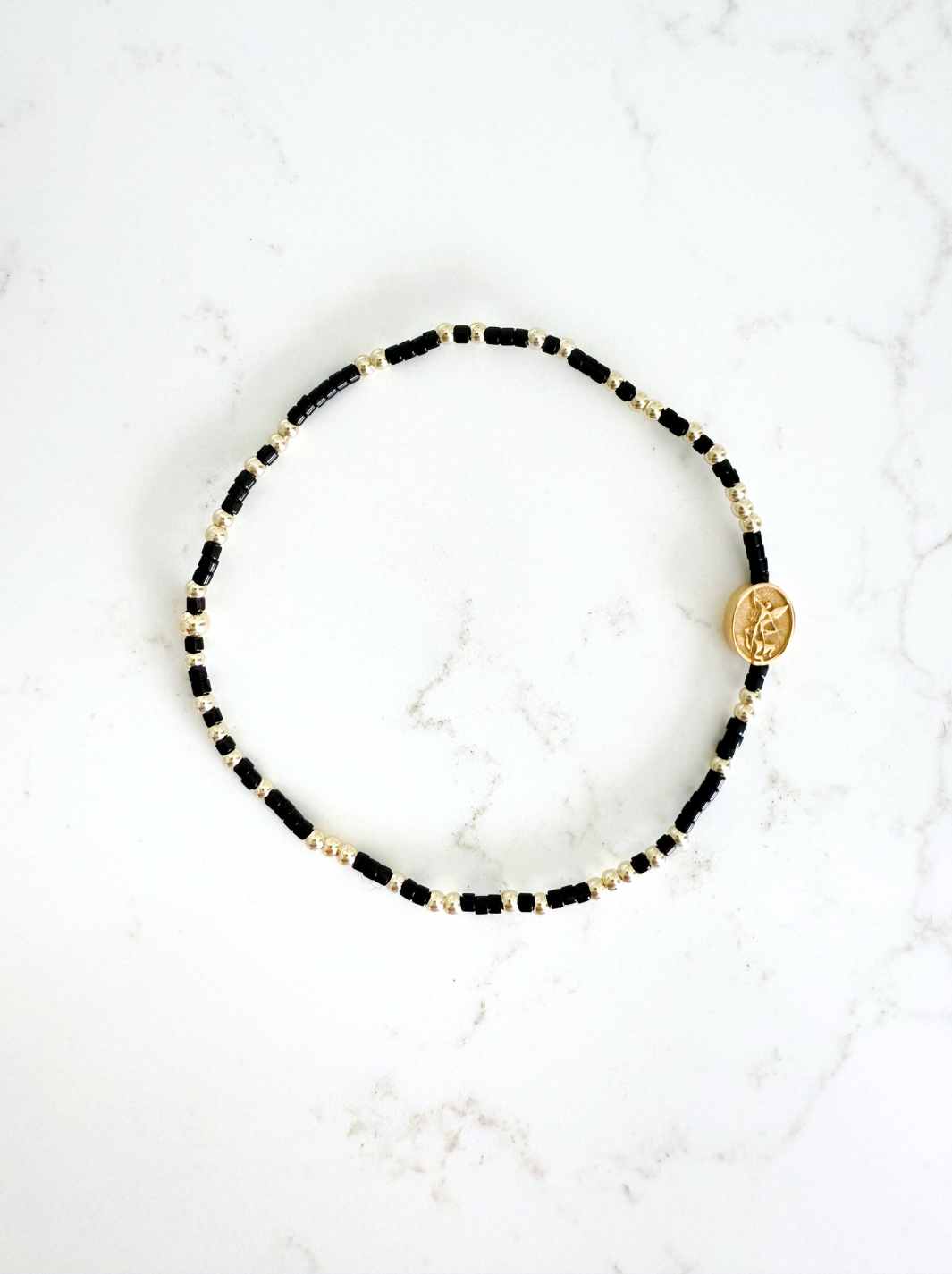 Bracelet with black and gold beads on a white marble surface