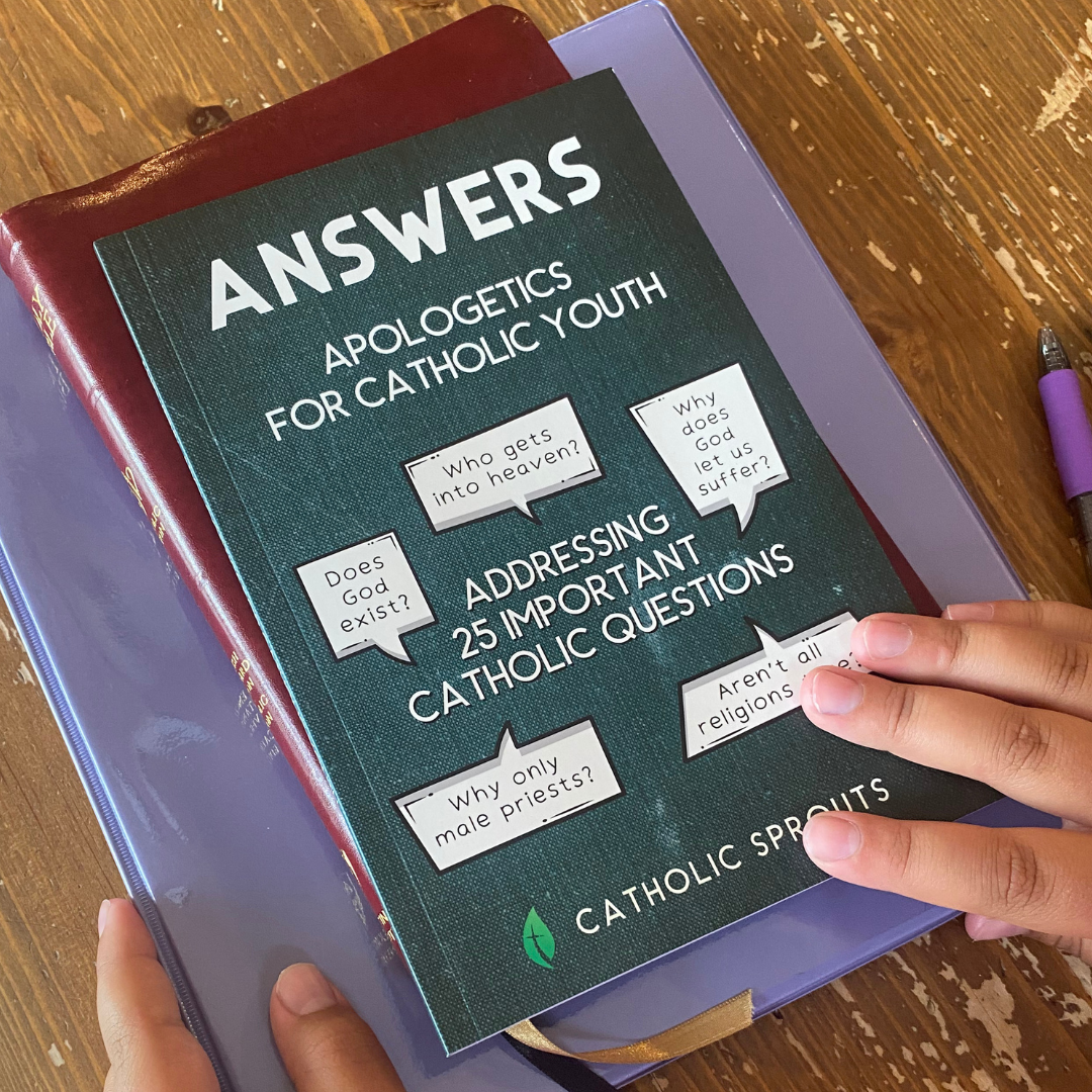 Book titled 'Answers Apologetics for Catholic Youth' on a wooden surface with hands holding it.