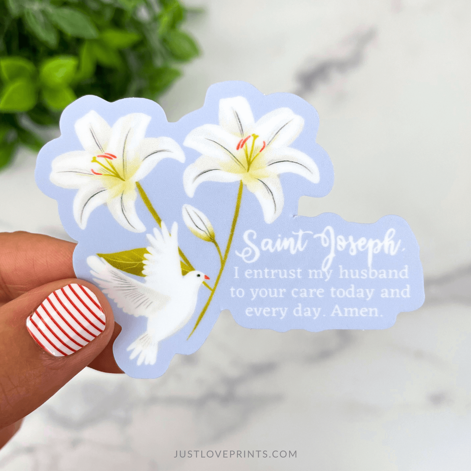 Sticker with white lilies, dove, and text held by a hand with striped nail polish.