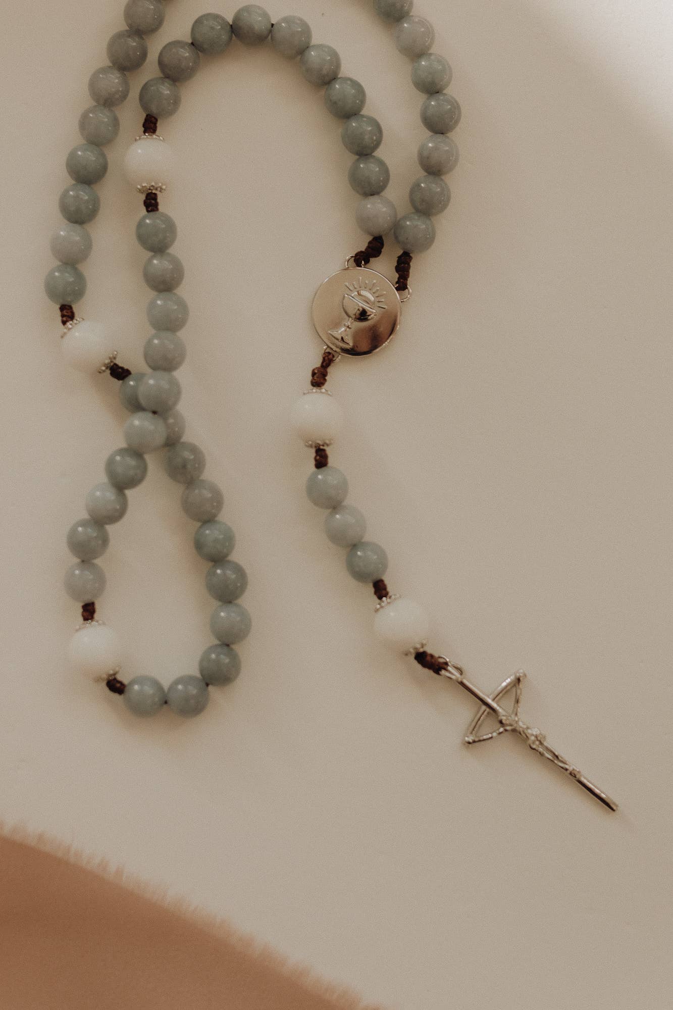 Rosary with gray beads and a silver cross on a light background