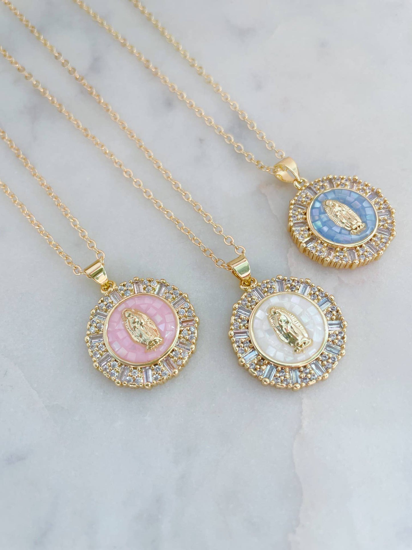 Three gold necklaces with circular pendants on a marble surface