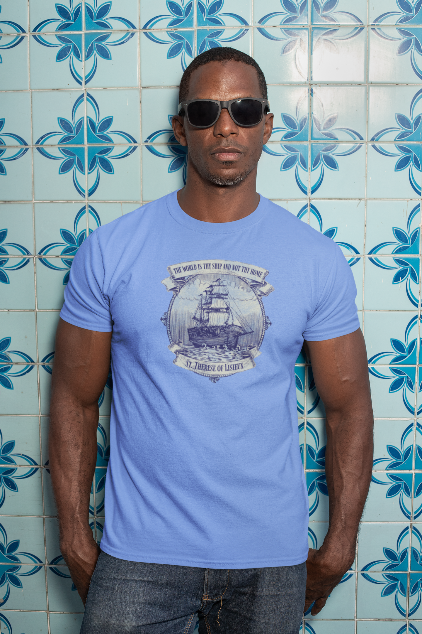Man wearing a light blue t-shirt with a graphic design against a blue tiled wall.