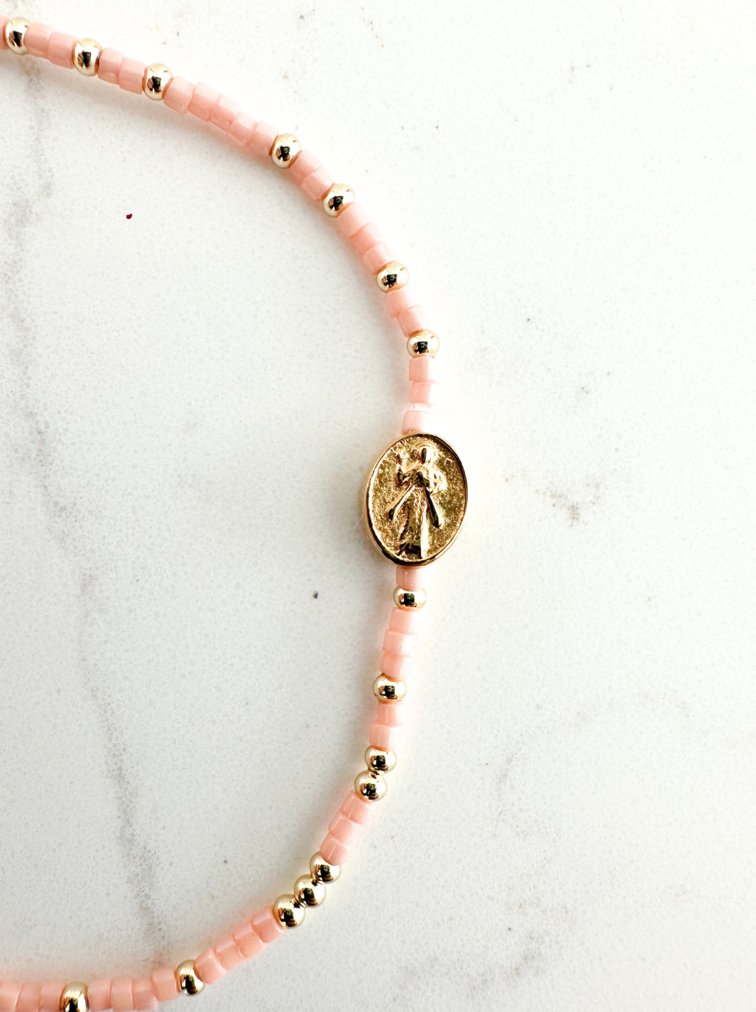Bracelet with pink beads and gold accents on a marble surface
