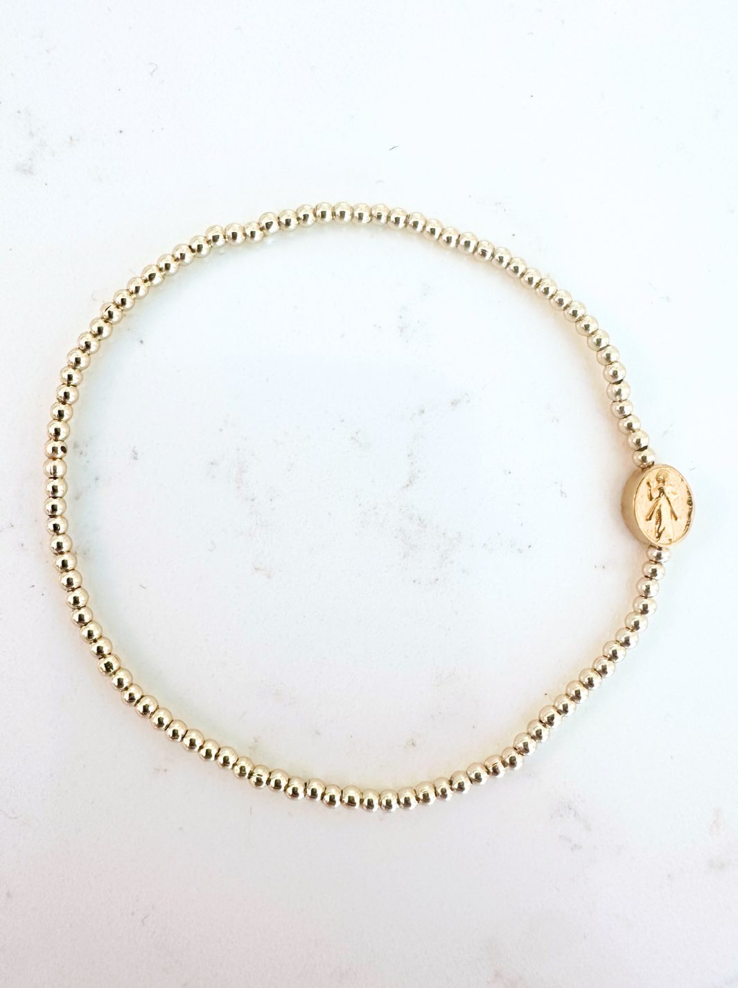 Gold beaded bracelet with a round charm on a light background