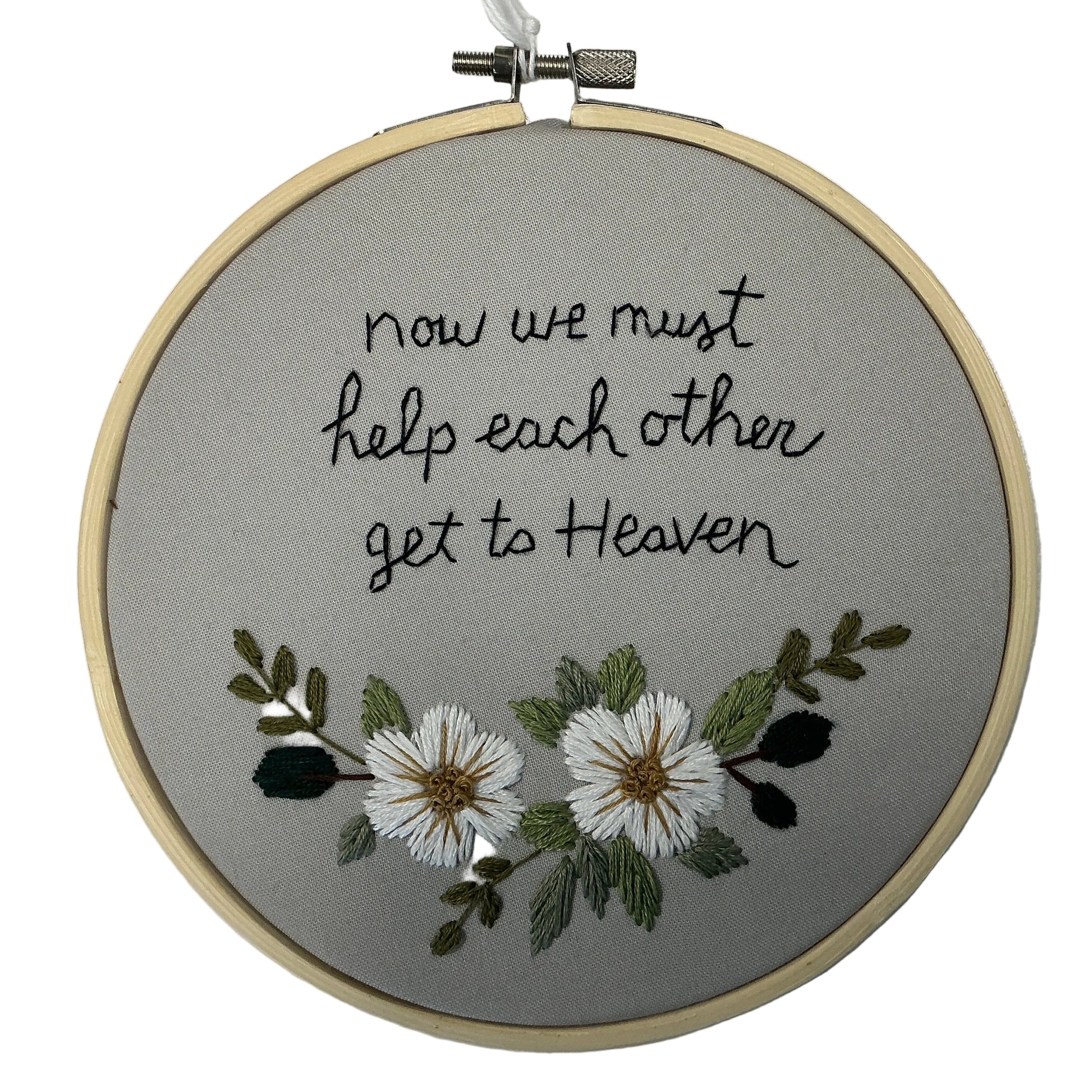 Embroidery hoop with text 'now we must help each other get to Heaven' and floral design on a gray background.