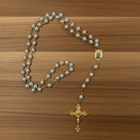 Pearl rosary with a gold cross on a wooden surface