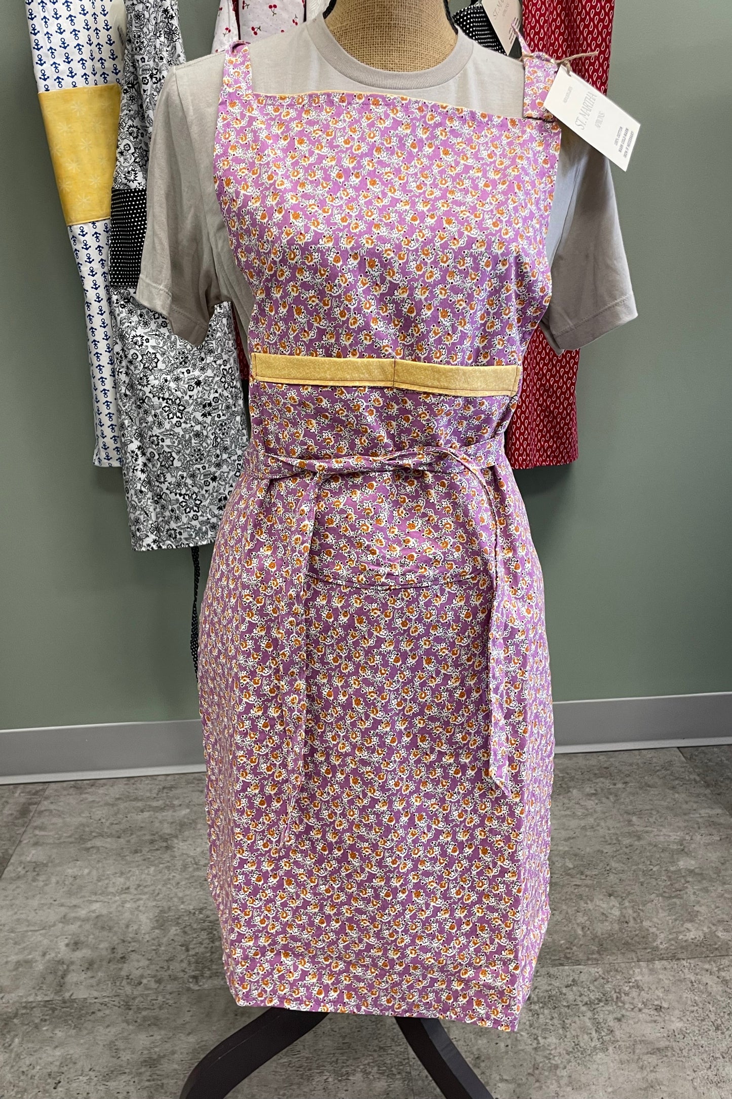 Purple floral apron with yellow accents on a rack against a gray wall.