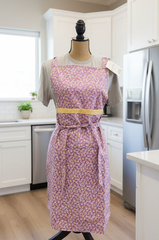 Purple floral apron with yellow accents on a rack against a gray wall.