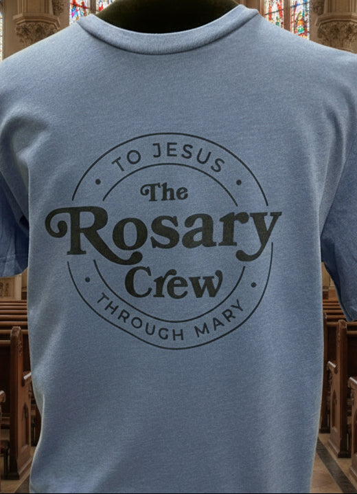 Blue shirt with 'The Rosary Crew' logo held by a person indoors.