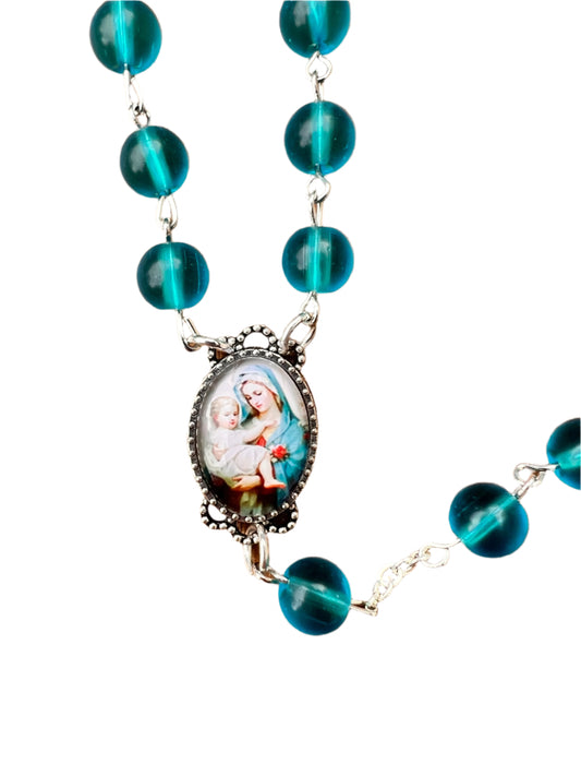 Rosary with blue beads and a central religious pendant of the Madonna and Child on a white background