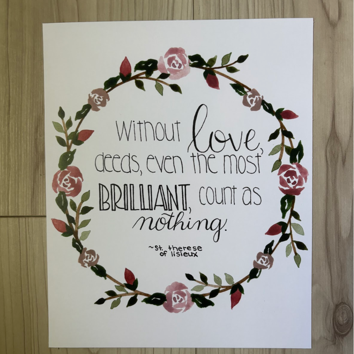 Print with floral design and text from St. Therese of Lisieux on a wooden surface