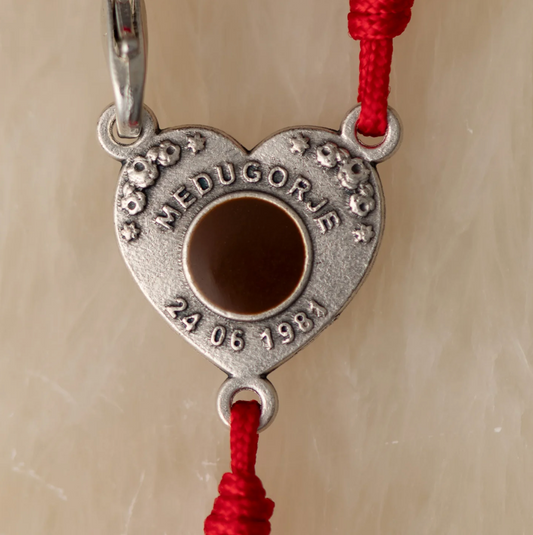 Heart-shaped metal pendant with red strings on a beige background