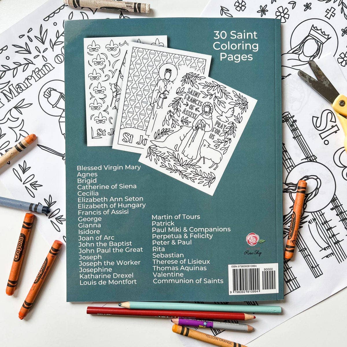Coloring book with 30 Saint Coloring Pages on a table with coloring supplies.