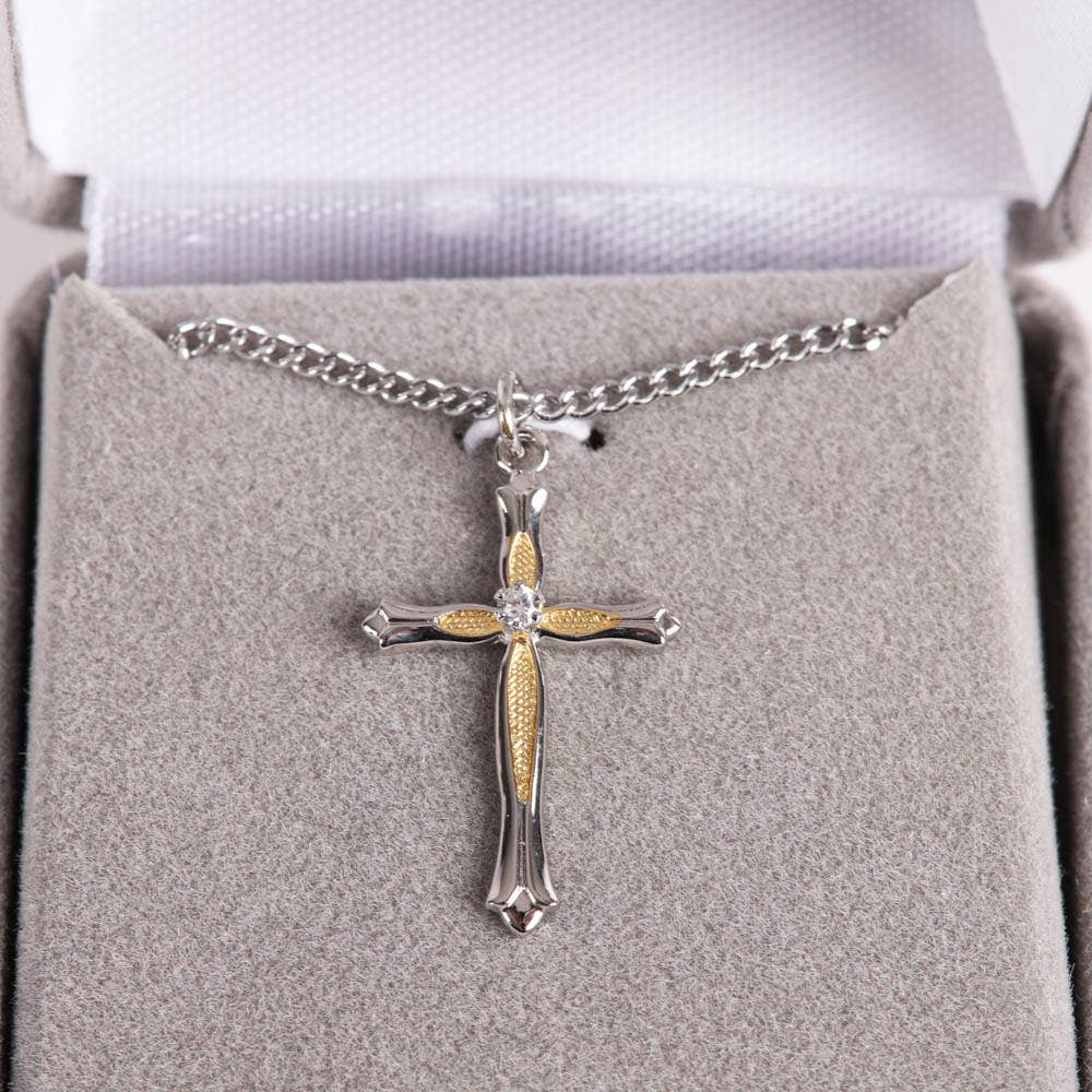 Silver and gold cross necklace on a gray cushion in a jewelry box