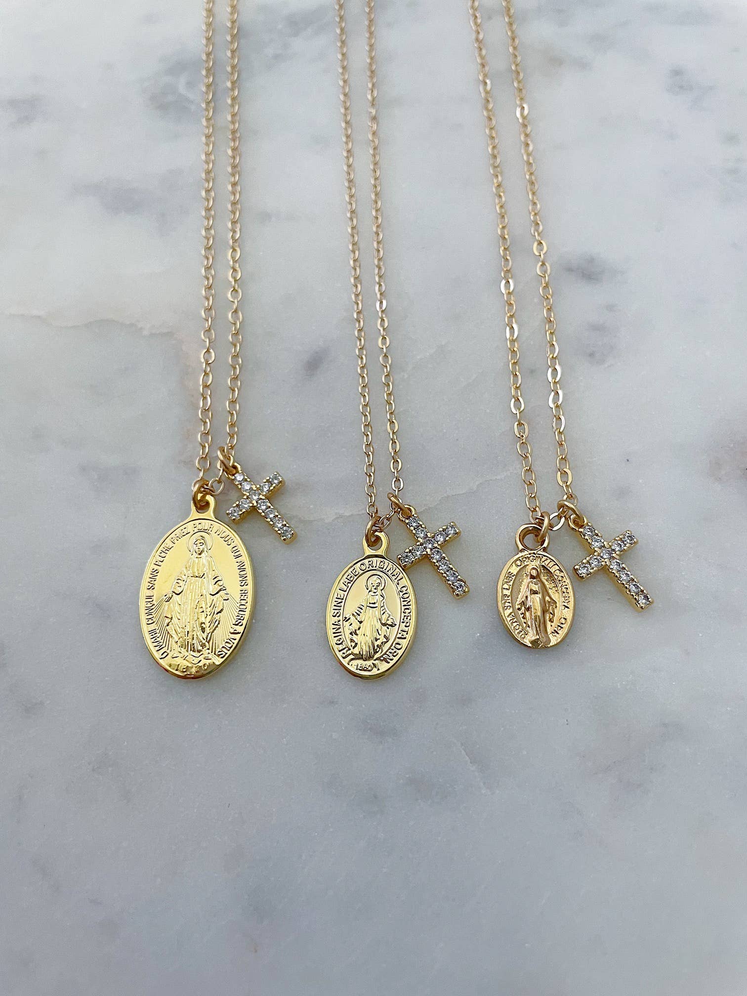 Three gold necklaces with religious pendants on a marble surface