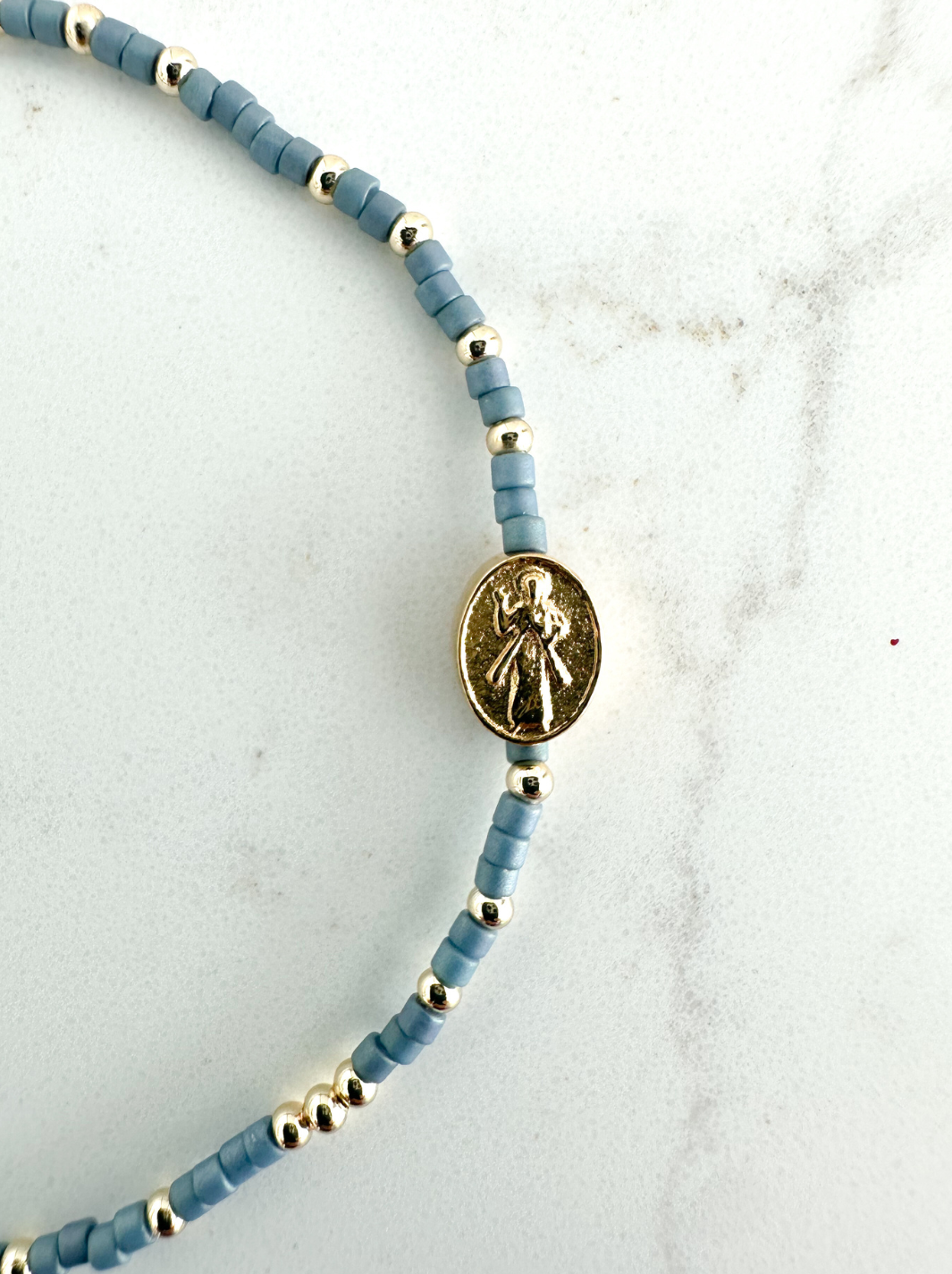 Bracelet with blue beads and a gold charm on a light gray background