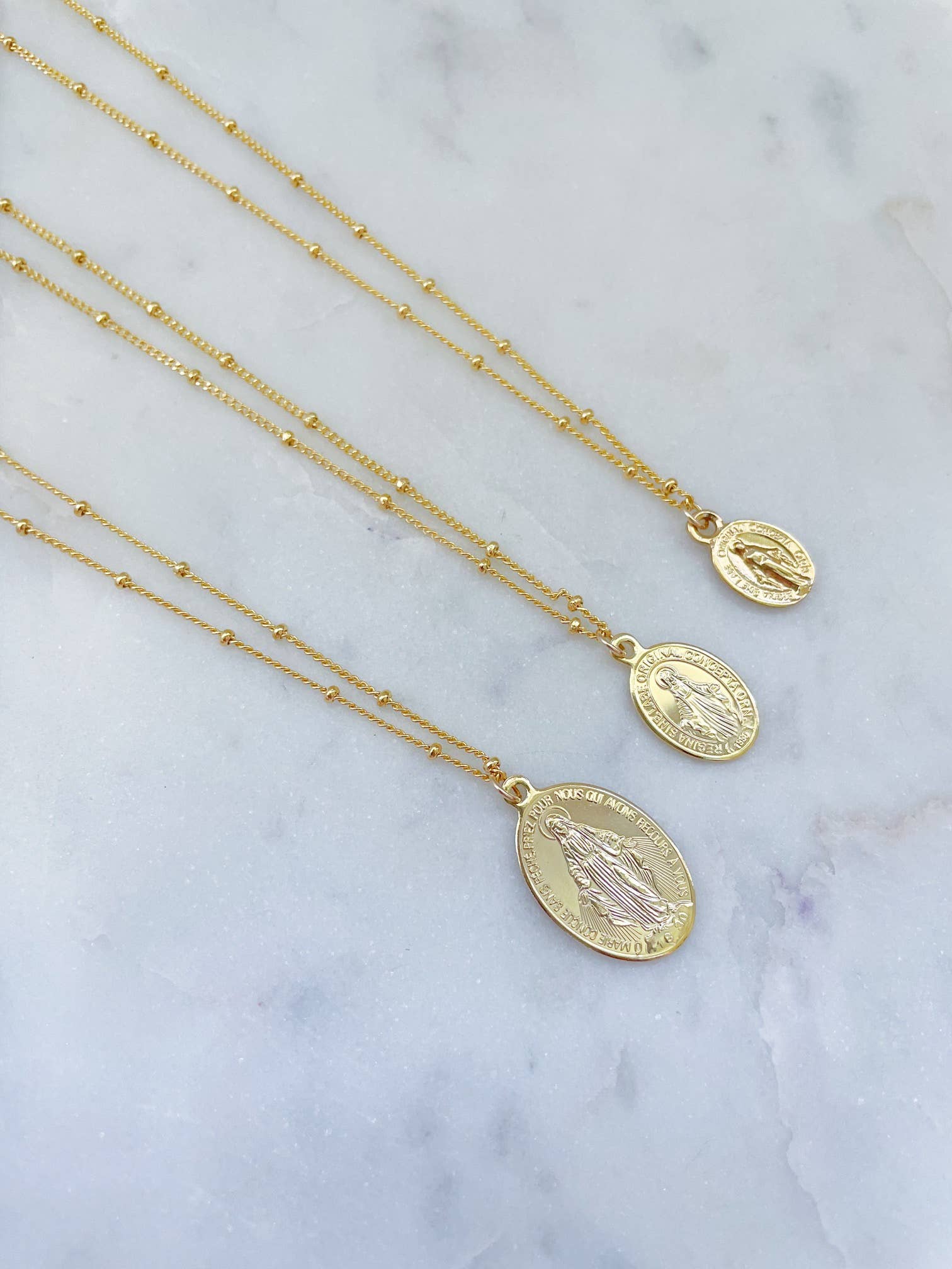 Gold necklaces with medallions on a marble surface