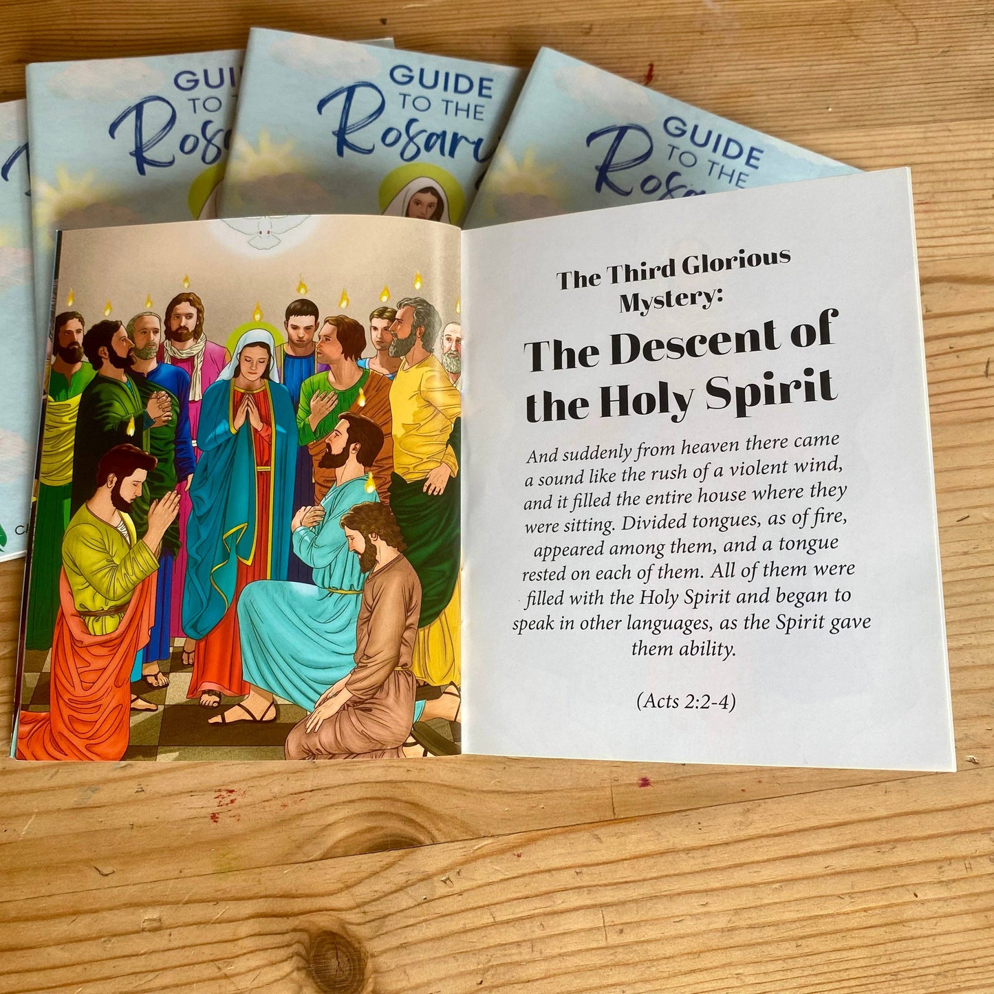 Open book about the Rosary with colorful illustrations on a wooden surface