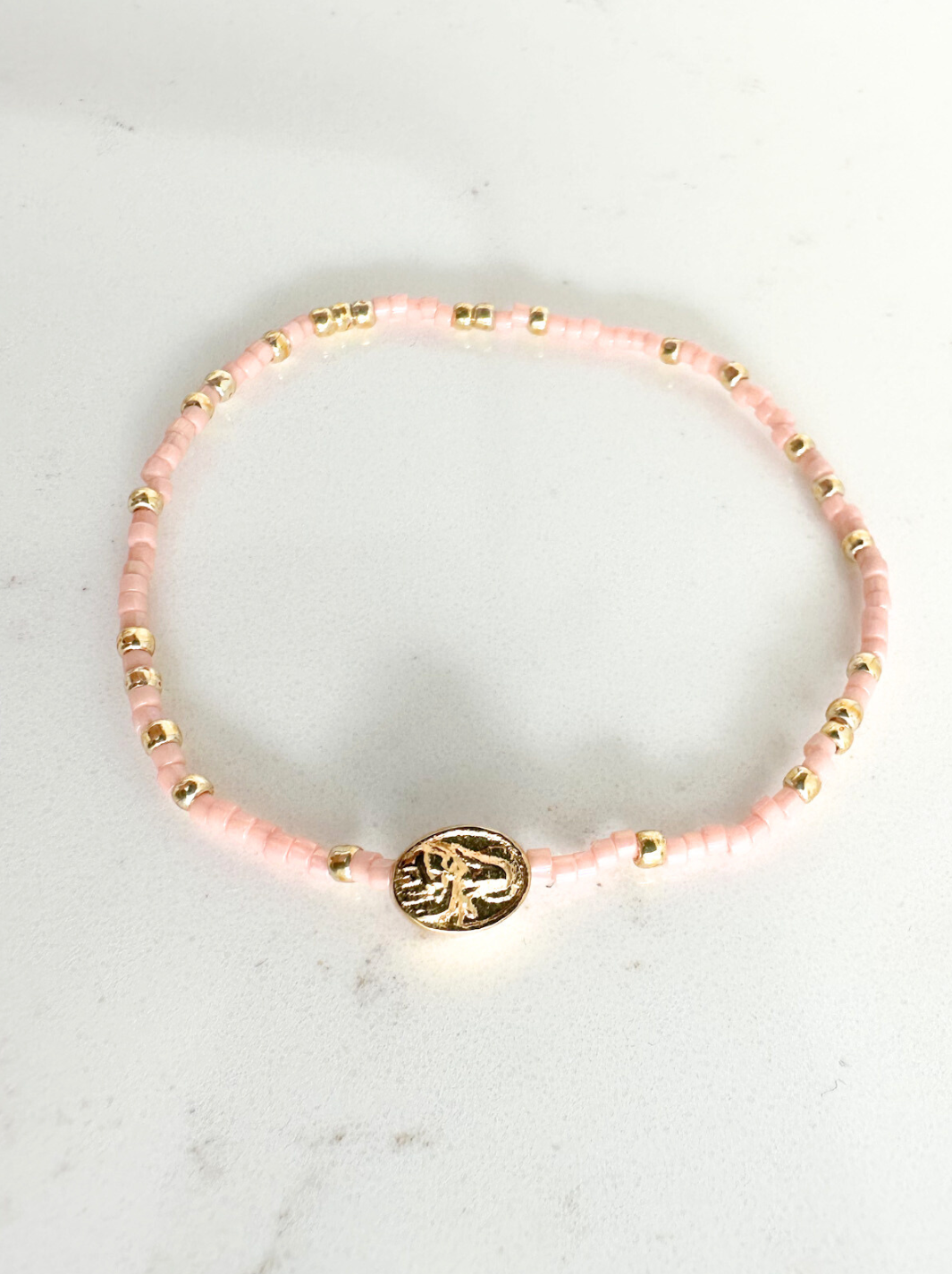 Pink beaded bracelet with a gold charm on a white marble surface