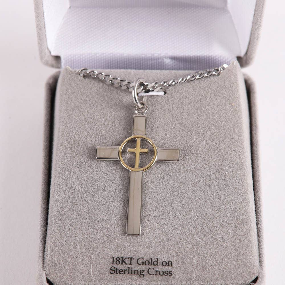 Silver cross pendant with gold circle on a chain in an open jewelry box.