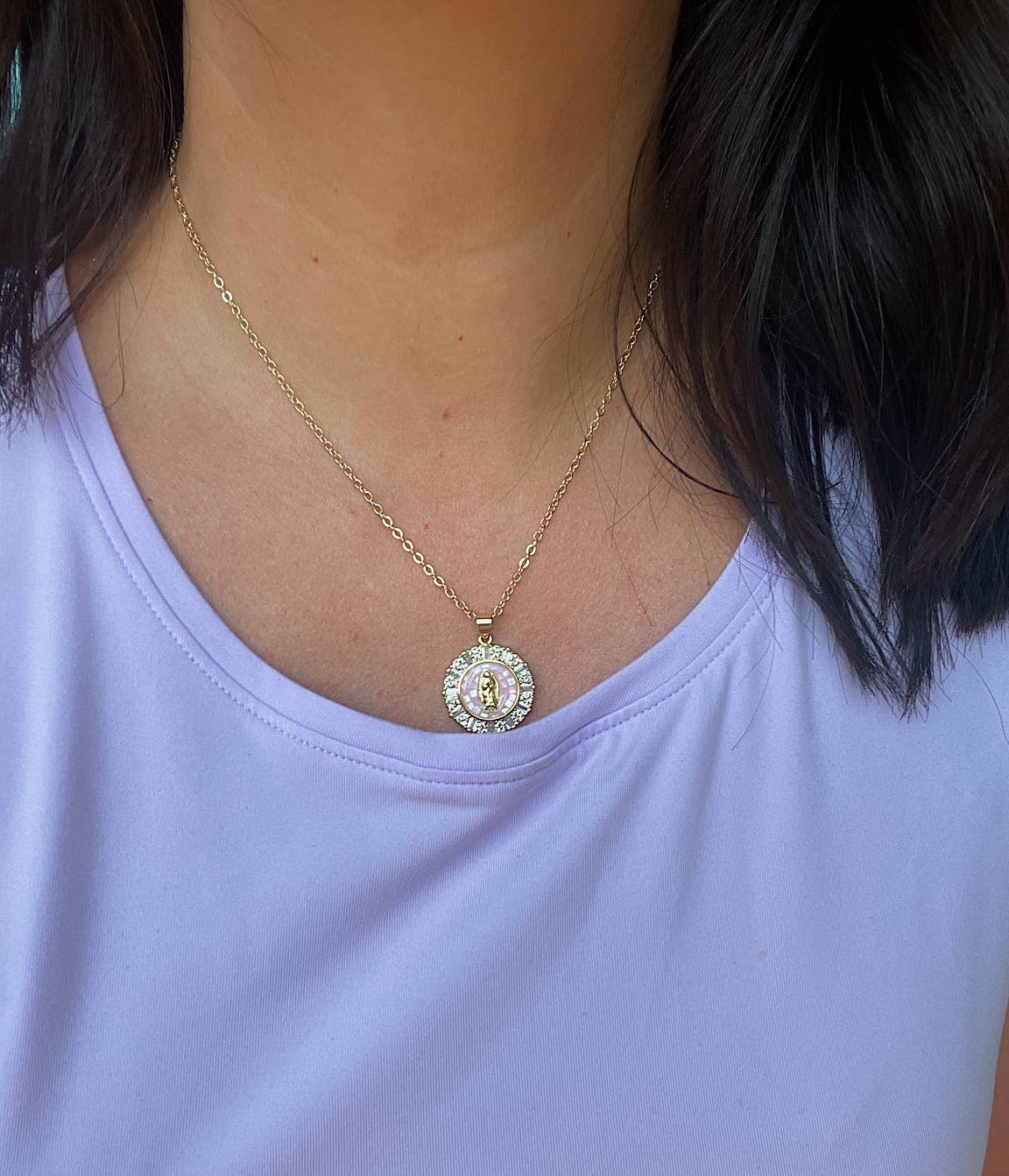 Necklace with a circular pendant worn by a person in a light purple shirt.