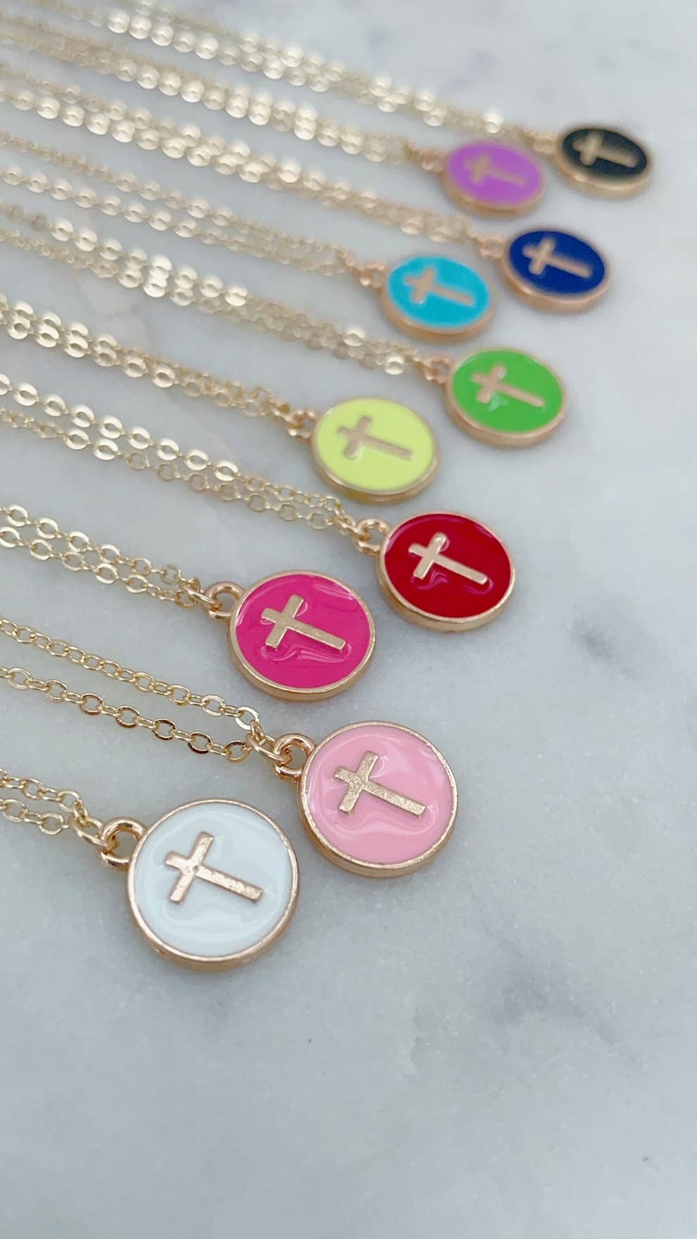 Necklaces with colorful circular pendants featuring crosses on a marble surface