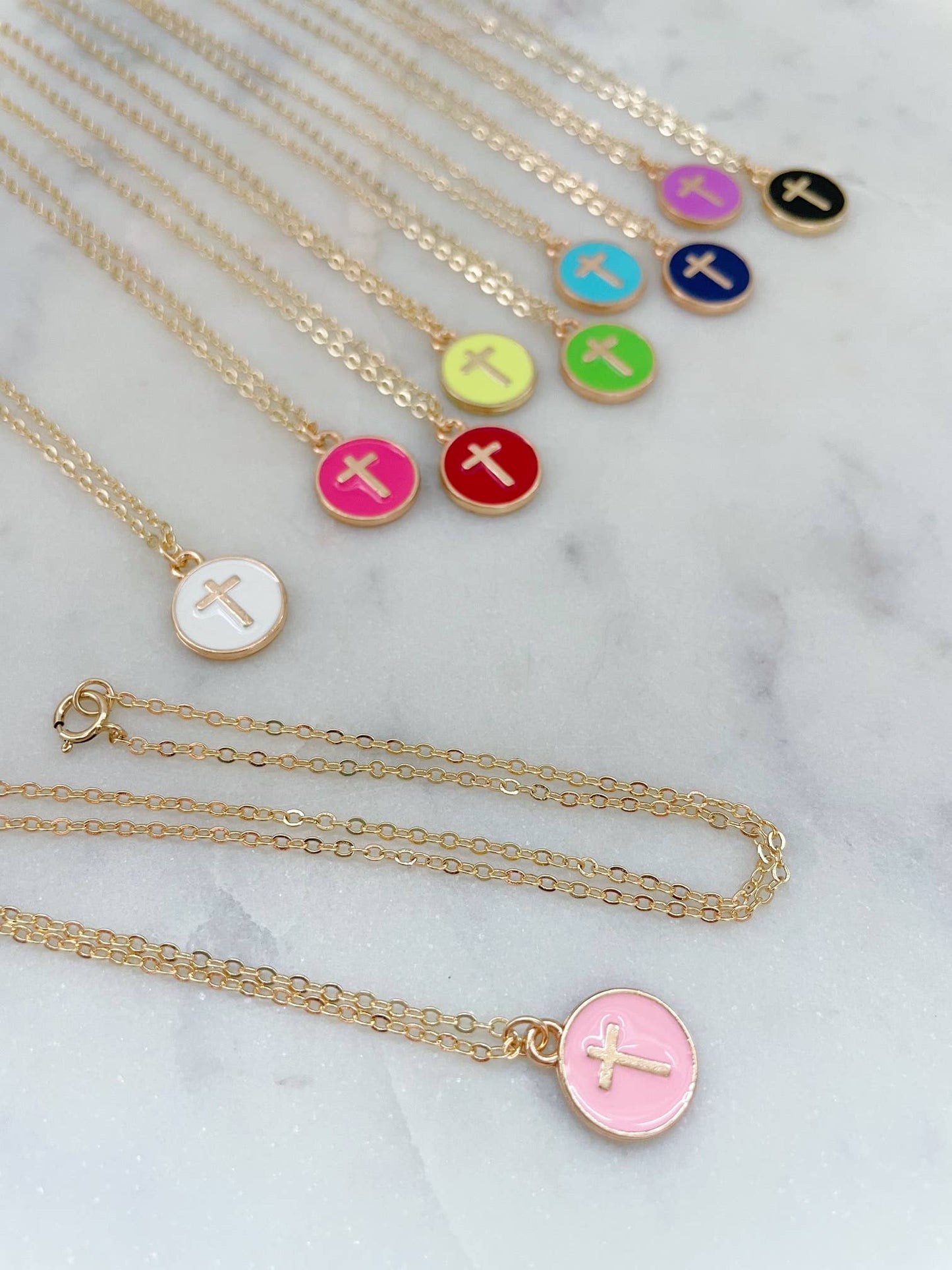 Necklaces with colorful disc pendants featuring crosses on a marble surface