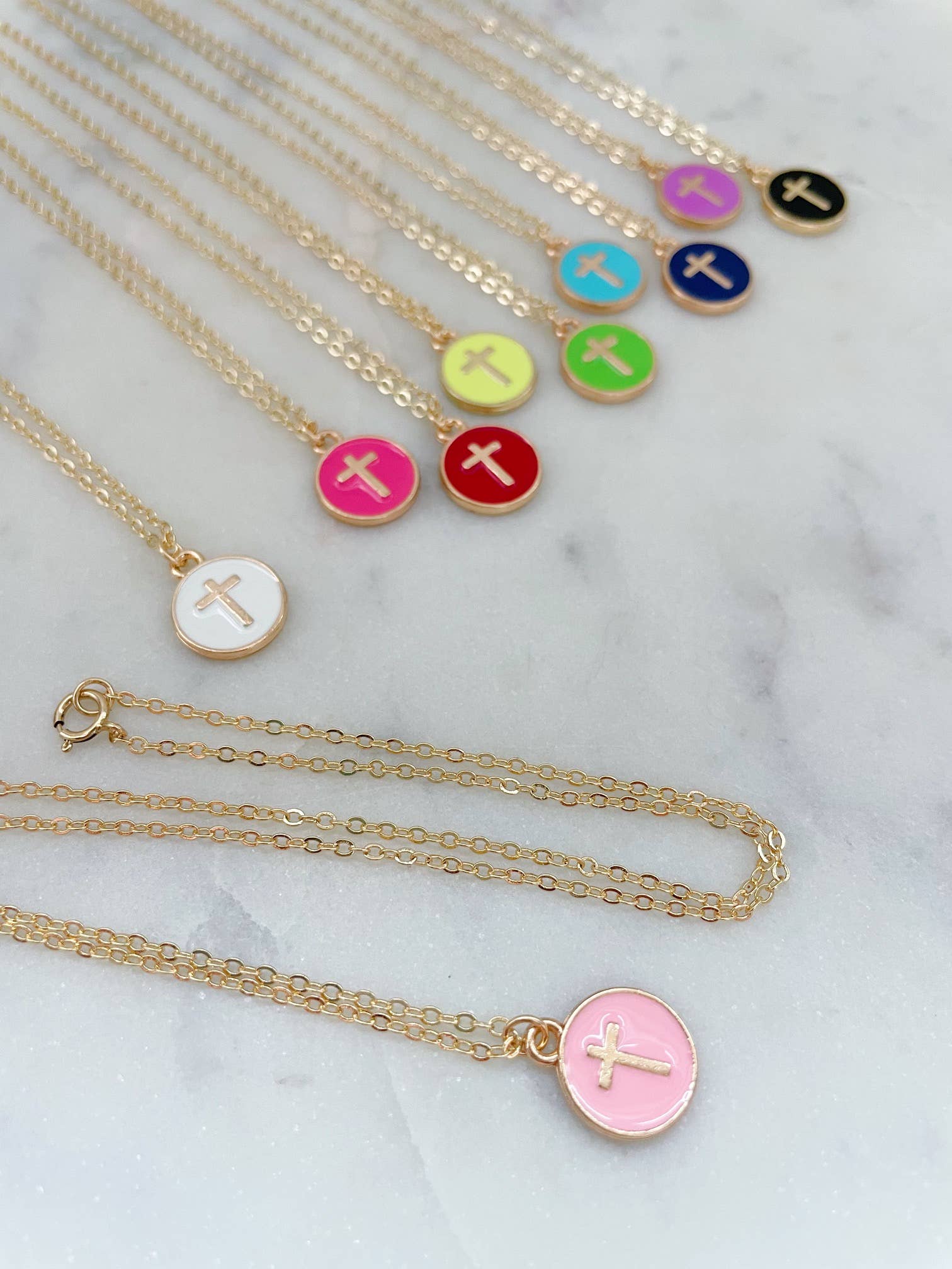 Necklaces with colorful disc pendants featuring crosses on a marble surface