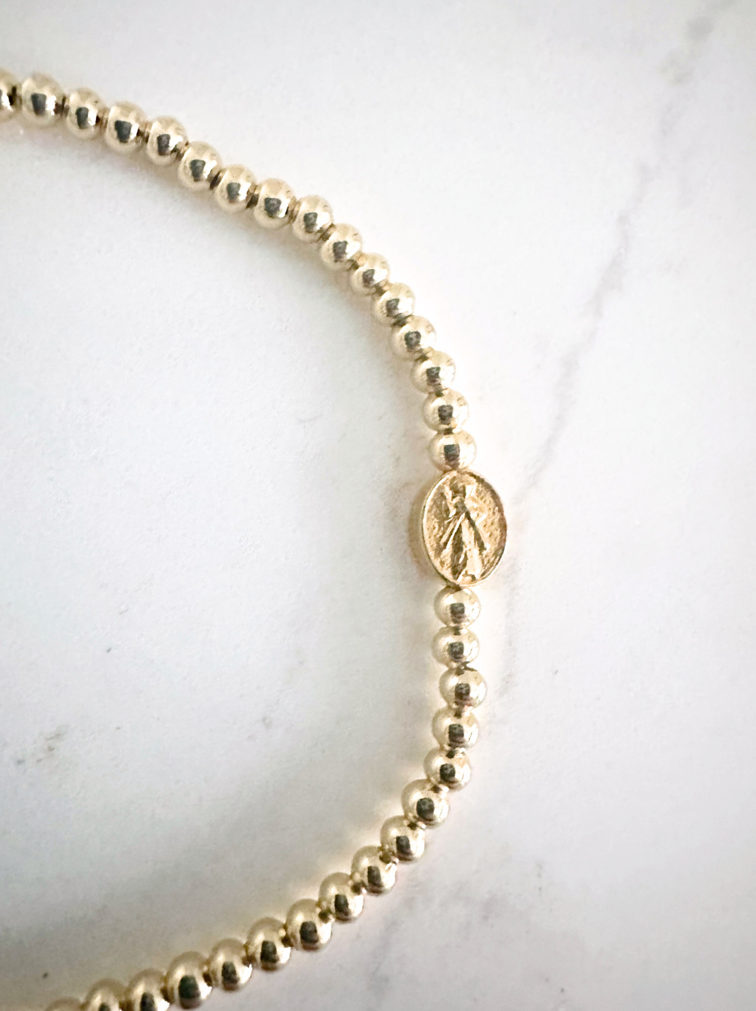 Gold beaded necklace with a charm on a white background