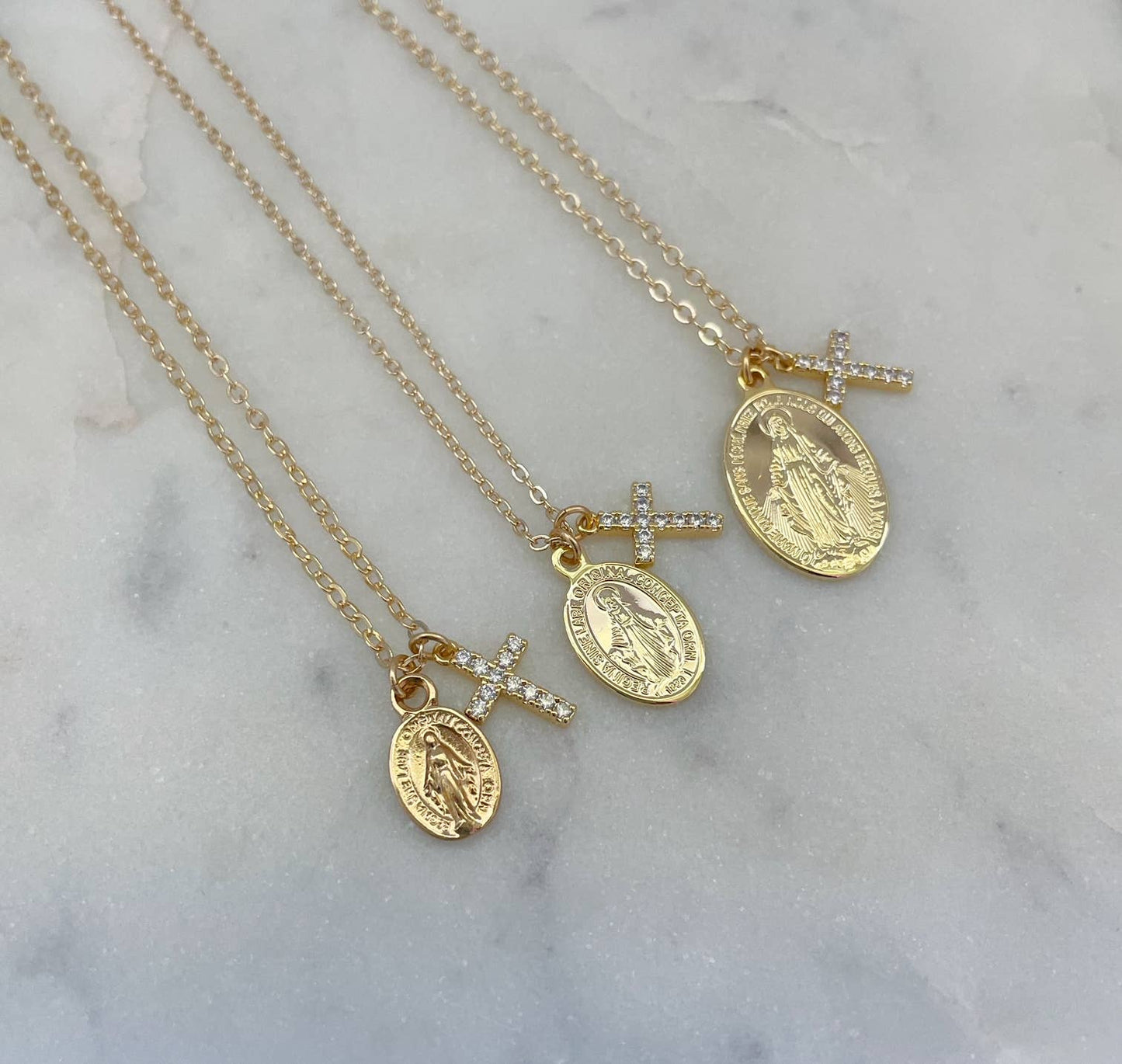 Three gold necklaces with religious pendants on a marble surface